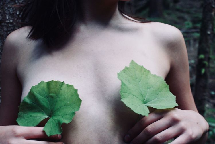 Midsection of shirtless woman covering breast with leaves