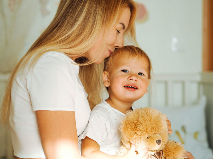 Young beautiful mother with long blond hair having fun with pretty baby boy at home