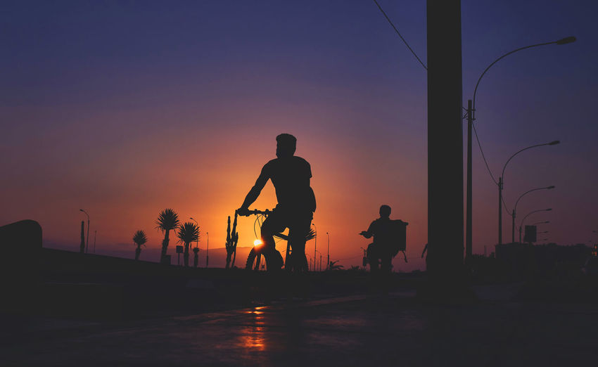 Silhouette people standing on street against sky during sunset