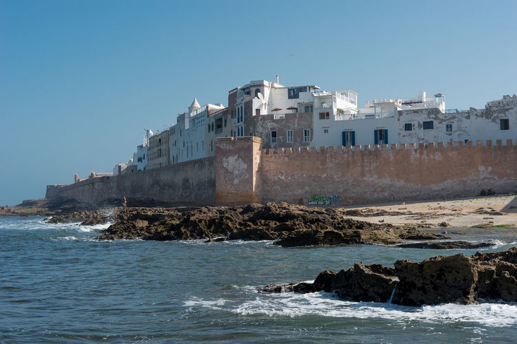 Buildings by sea against clear sky