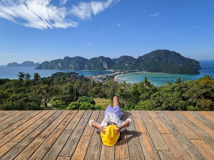 Rear view of woman sitting on pier over sea against sky