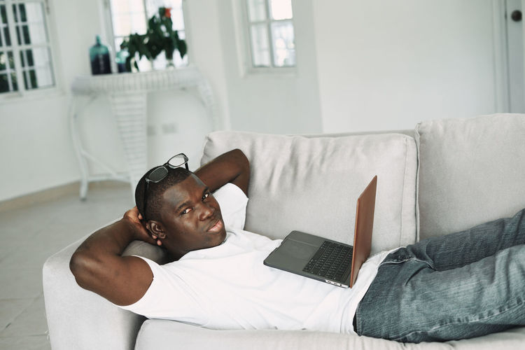 Portrait of man with laptop lying on sofa at home