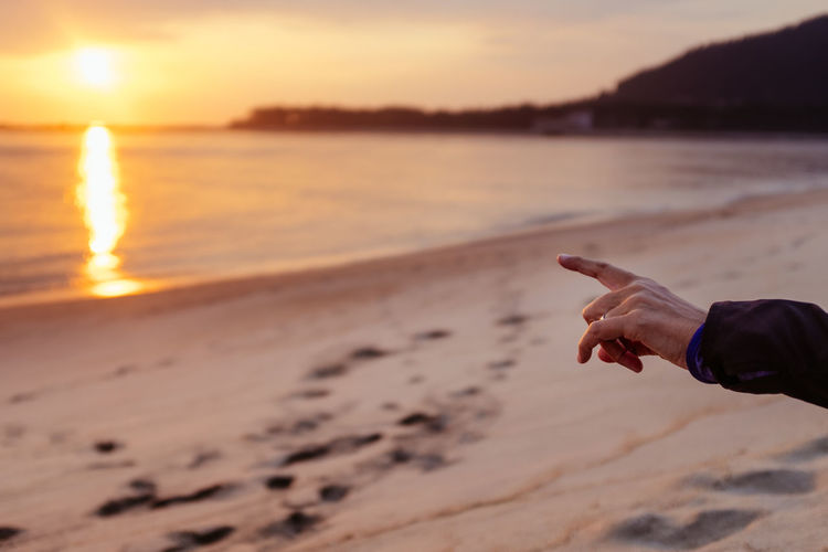 Cropped hand pointing at beach during sunset