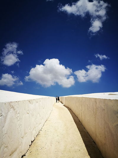 Rear view of woman walking on road against blue sky
