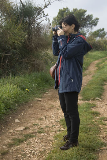 Full length of woman photographing with the camera while standing on the field