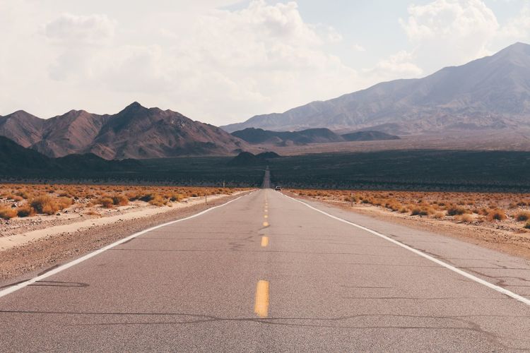 Road leading towards mountains against sky