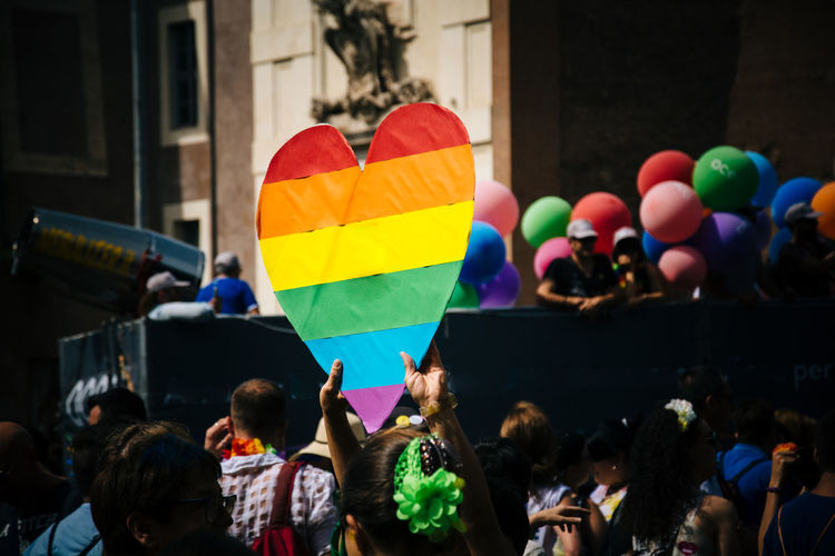 Man holding heart shape rainbow flag amidst people during gay pride parade