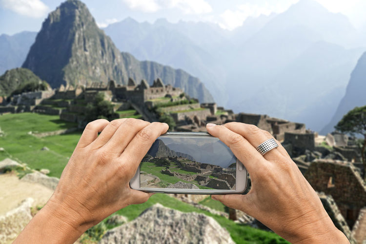 Cropped hands photographing old ruin at machu picchu with smart phone