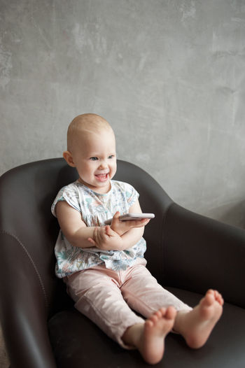 Funny smiling child with phone sits on chair. alpha generation concept