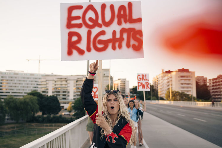 Women with poster shouting while marching for equal rights on bridge in city