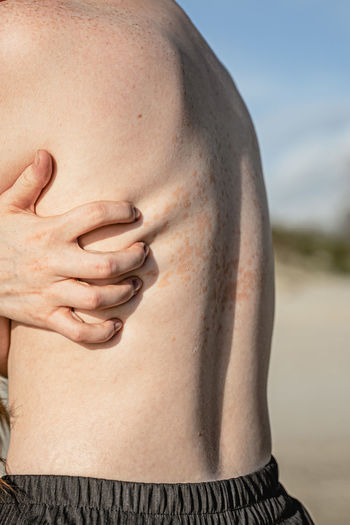 Midsection of woman scratching back at beach