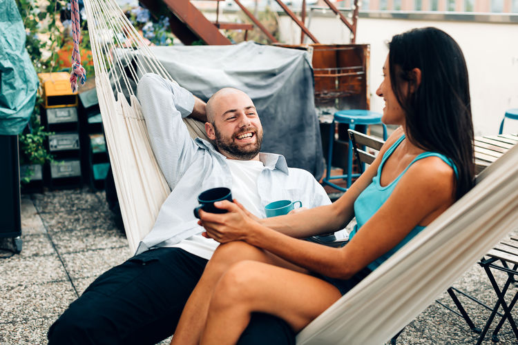 Friends colleagues couple relaxing cuddling in a hammock holding a cup of tea or coffee