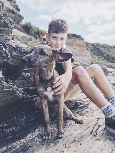 Portrait of boy with dog sitting on land against sky