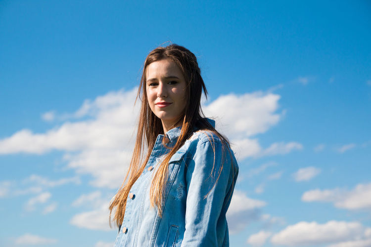 Portrait of young woman standing against blue sky