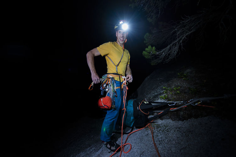 Man finishing rock climbing at night with headlamp top of climb