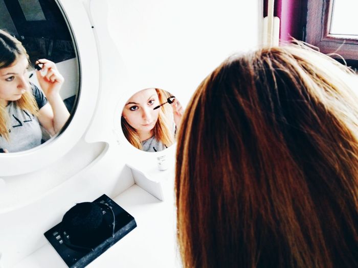 Reflection of woman in mirror while applying mascara at home
