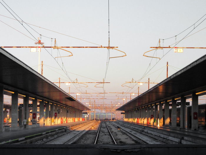 Electricity cables over railroad tracks amidst stations against sky