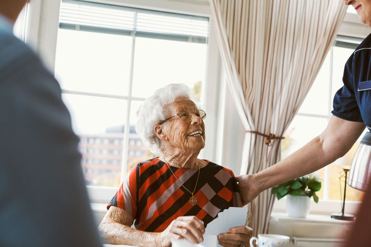 Happy senior woman looking at caretaker while playing cards with family