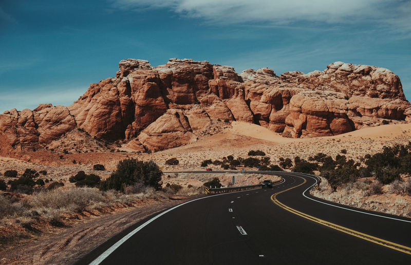 Car on road leading towards rock formation against sky