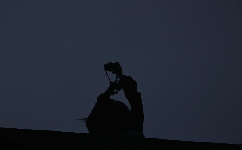 Silhouette man holding camera against sky at night