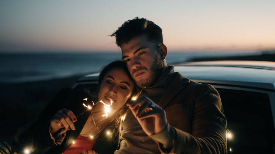 Couple embracing while holding sparkler at dusk