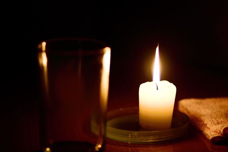 Close-up of illuminated candle by glass on table