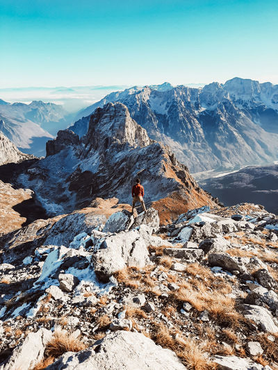 Midsection of person on rock by snowcapped mountain against sky