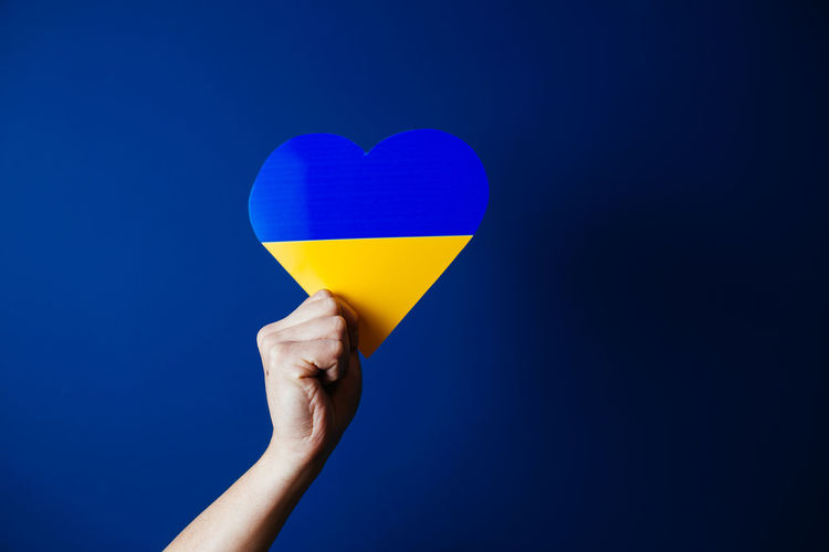 Cropped hand holding heart shape against blue background