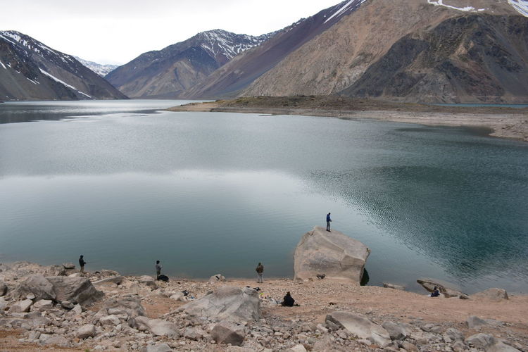 People fishing in lake against mountains