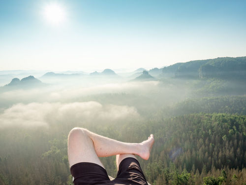 First person view to resting hiking legs,resting during hike. high rocks, clear sky and sun,