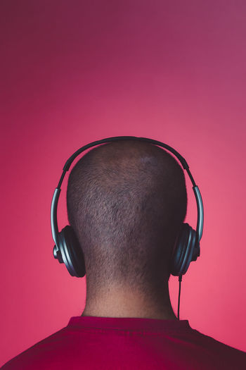 Rear view of man listening music against red background