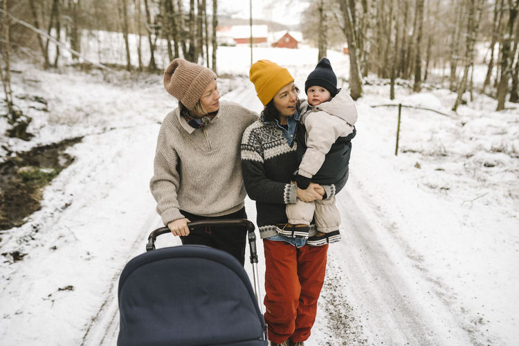 Mature woman carrying daughter while walking with girlfriend on snow