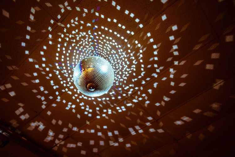 Low angle view of illuminated disco ball hanging from ceiling in nightclub