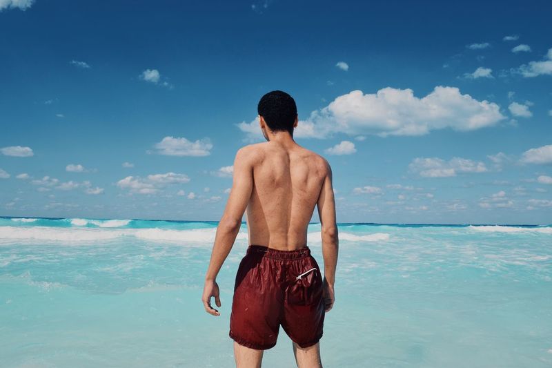 Rear view of shirtless man standing at beach