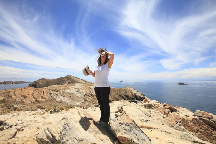 Full length woman standing on rock formation by lake titicaca against sky