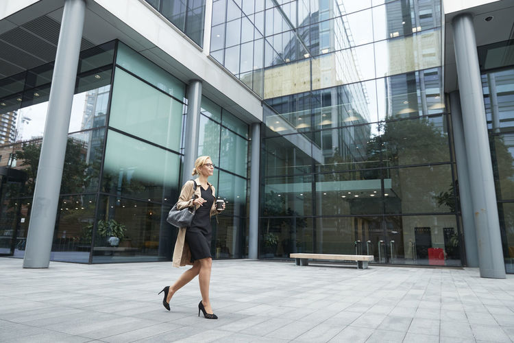 Woman holding coffee cup while walking against office building