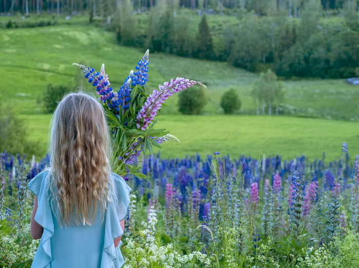 Rear view of woman standing by purple flowers on field