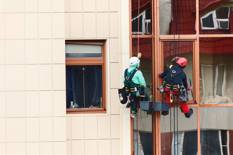 Two men hanging on the rope and washing windows . profession at risk