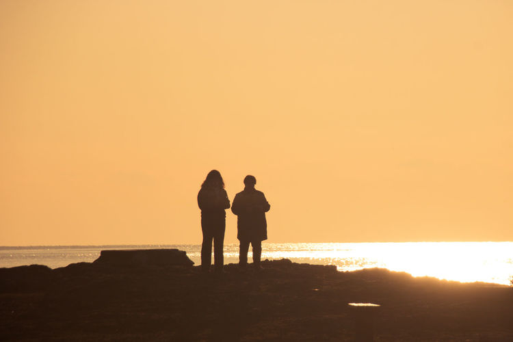 Silhouette man and woman on beach against sky during sunset