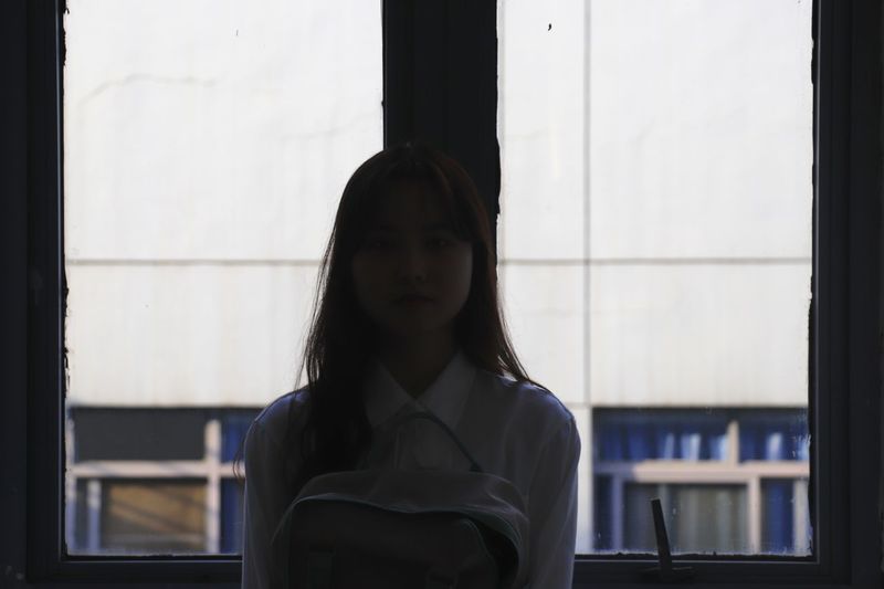 Portrait of young woman standing against window
