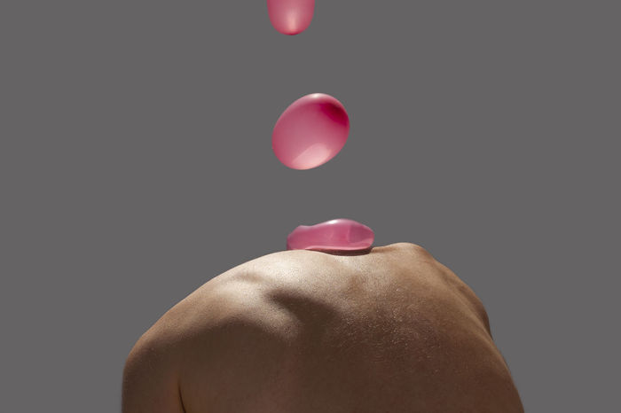 Water balloon falling on shirtless person against gray background