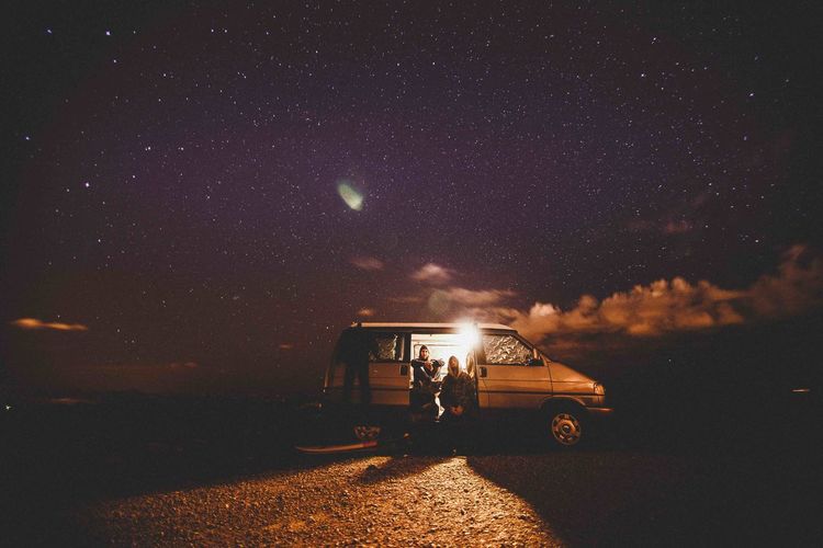 Friends sitting in car on land against starry sky at night