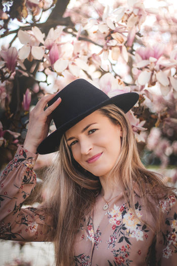 Natural smile of a young lady in a black hat under the flowering trees on a sunny summer day person