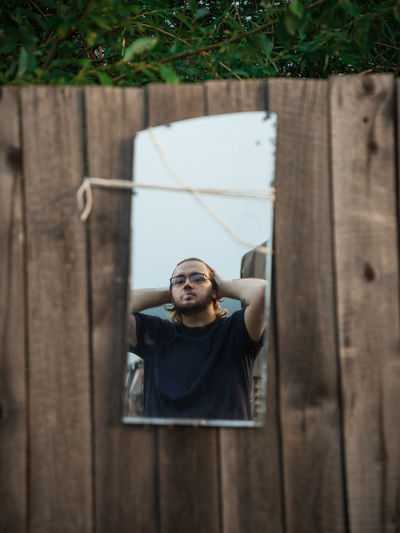 Portrait of a young man in the mirror on a wooden fence