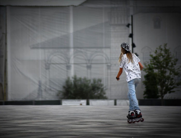 Rear view of young woman skating on street in city