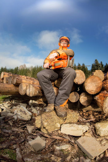 Low angle view of lumberjack sitting on wood against sky