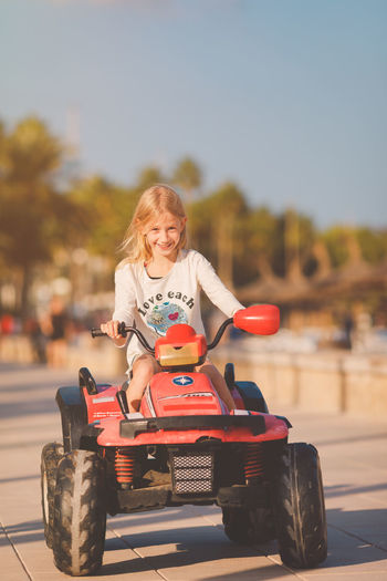 Portrait of girl riding toy car on footpath