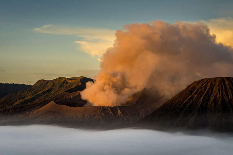 Smoke emitting from volcanic mountain against sky during sunset