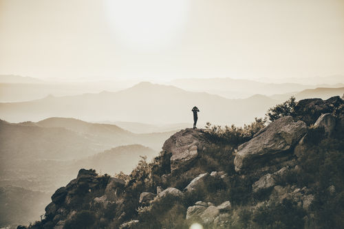 Mid distance view of woman standing on rocks against mountains and clear sky