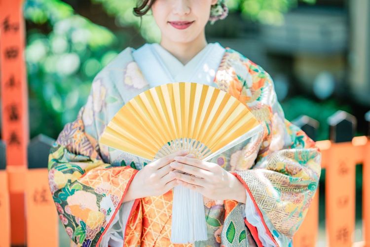 Midsection of woman wearing kimono and holding folding fan while standing outdoors